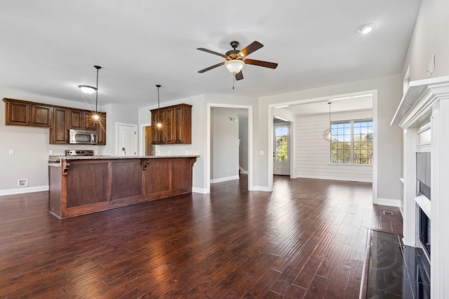 kitchen featuring a ceiling fan, stainless steel microwave, dark wood-type flooring, baseboards, and a peninsula
