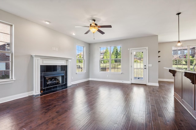 unfurnished living room with ceiling fan, baseboards, a tile fireplace, and dark wood-style floors