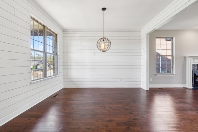 unfurnished dining area featuring dark wood finished floors, a healthy amount of sunlight, and wooden walls