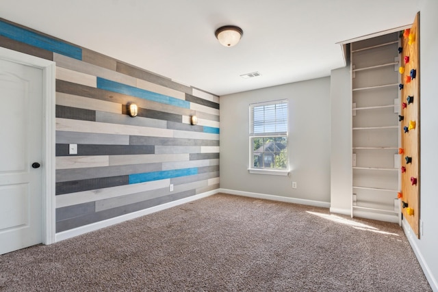 carpeted empty room with wooden walls, visible vents, and baseboards