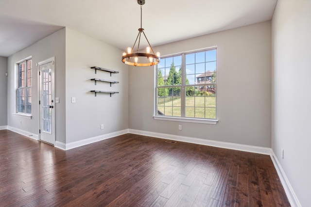 unfurnished dining area featuring dark wood finished floors, baseboards, and an inviting chandelier