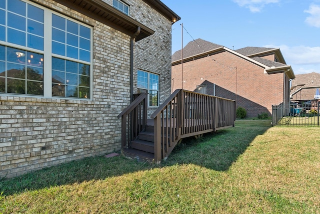 rear view of house with brick siding, a lawn, fence, and a deck