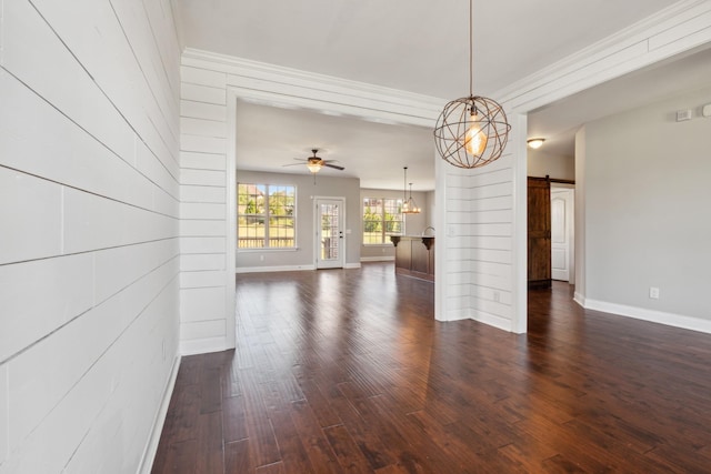 unfurnished dining area with a barn door, crown molding, ceiling fan, baseboards, and dark wood-type flooring