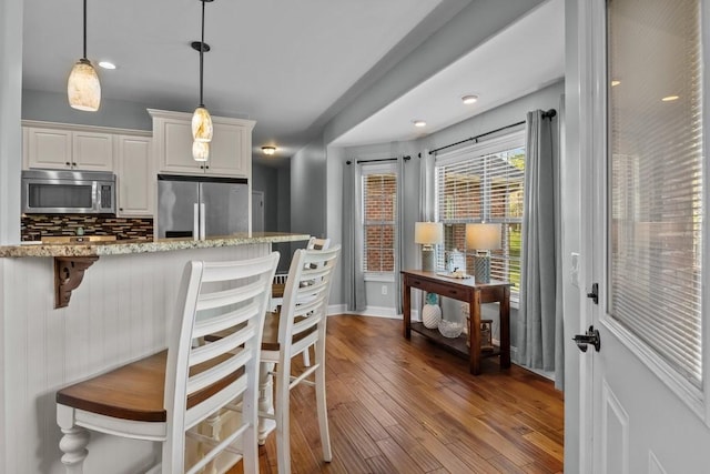 kitchen with stainless steel appliances, tasteful backsplash, wood finished floors, light stone counters, and a breakfast bar area