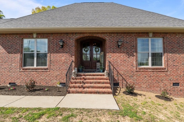 view of exterior entry with brick siding, french doors, roof with shingles, and crawl space