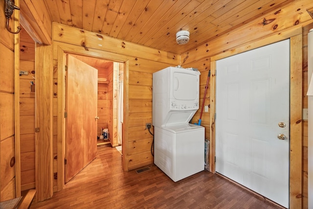 washroom featuring stacked washer / dryer, laundry area, wooden walls, visible vents, and dark wood-style flooring