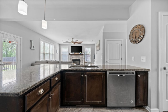 kitchen featuring stainless steel dishwasher, a sink, dark brown cabinets, a ceiling fan, and a stone fireplace