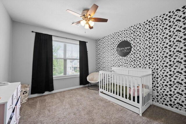 carpeted bedroom featuring a nursery area, an accent wall, baseboards, and ceiling fan