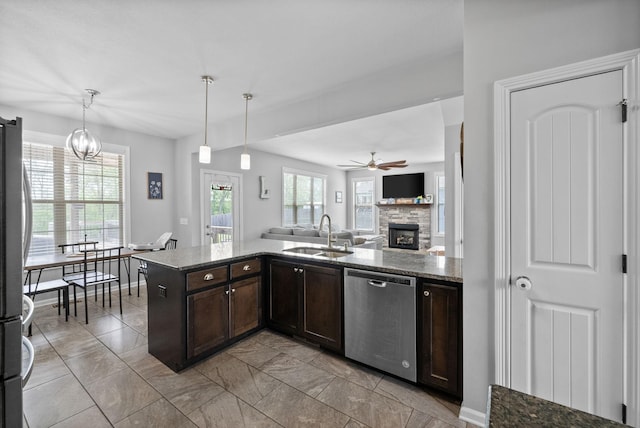 kitchen with stainless steel appliances, dark brown cabinets, a stone fireplace, a sink, and open floor plan