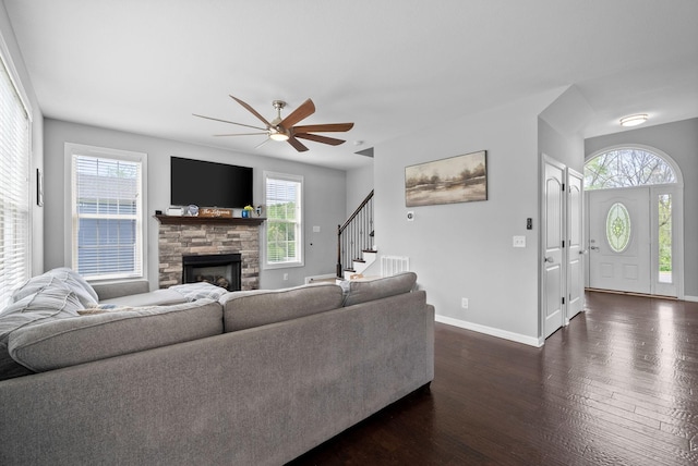 living area featuring a stone fireplace, a healthy amount of sunlight, ceiling fan, and dark wood-style flooring