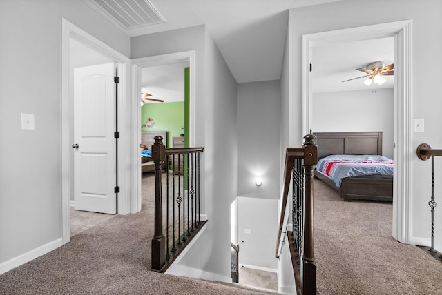 hall with visible vents, carpet flooring, baseboards, and an upstairs landing