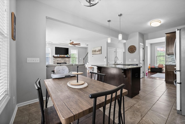 dining area featuring plenty of natural light, baseboards, a ceiling fan, stairs, and a stone fireplace