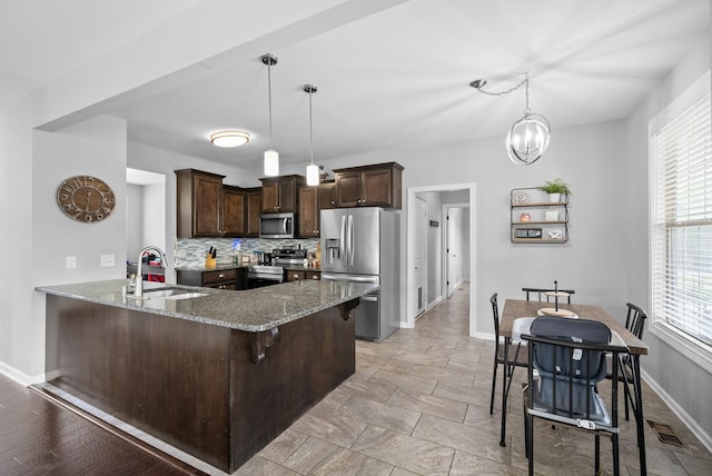 kitchen featuring a peninsula, a sink, stone counters, dark brown cabinetry, and appliances with stainless steel finishes