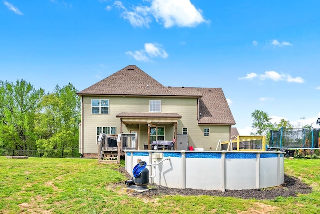 rear view of house featuring a wooden deck, a trampoline, ceiling fan, a yard, and an outdoor pool
