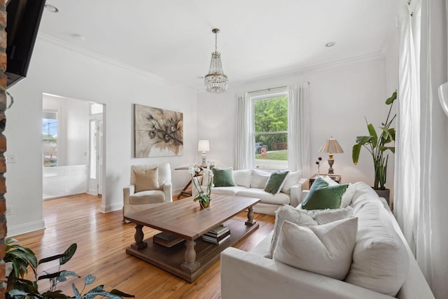 living area with light wood-style flooring, ornamental molding, baseboards, and a notable chandelier