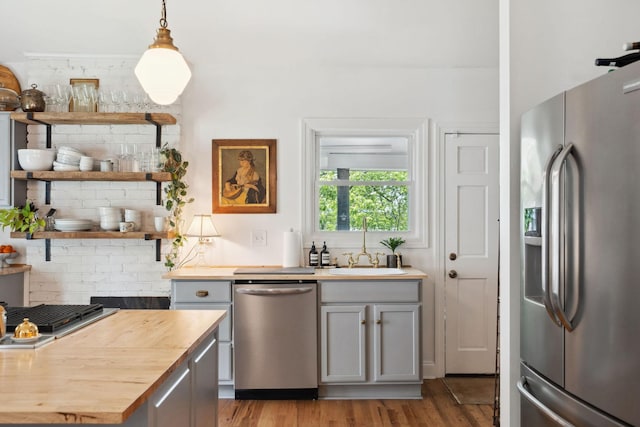 kitchen featuring stainless steel appliances, light wood-style flooring, a sink, decorative backsplash, and wood counters
