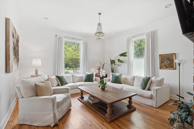 living room with an inviting chandelier, crown molding, light wood finished floors, and baseboards