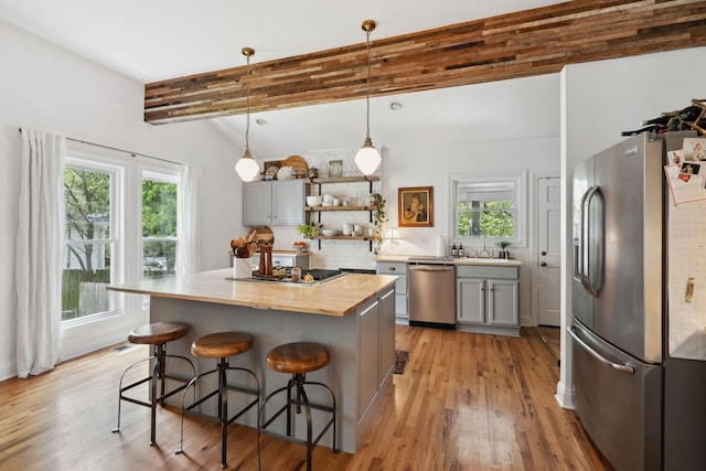 kitchen with open shelves, butcher block counters, gray cabinetry, a kitchen bar, and appliances with stainless steel finishes