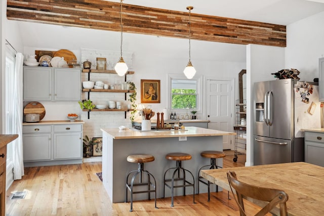 kitchen with light wood finished floors, stainless steel fridge with ice dispenser, gray cabinetry, hanging light fixtures, and a breakfast bar area