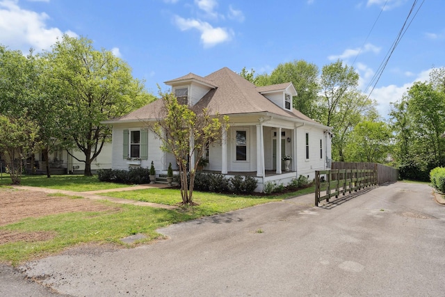 view of front of house with roof with shingles, a porch, a front yard, and fence