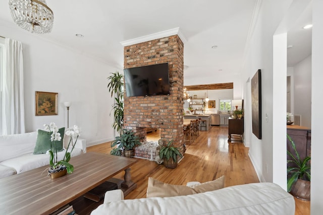 living area featuring a notable chandelier, baseboards, crown molding, and light wood finished floors