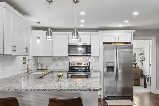 kitchen featuring dark wood finished floors, stainless steel appliances, a sink, a peninsula, and white cabinetry