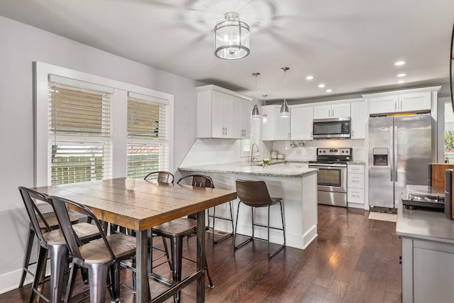 kitchen featuring dark wood-style flooring, a sink, white cabinets, a peninsula, and appliances with stainless steel finishes