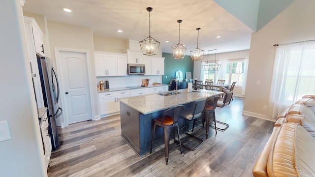 kitchen featuring stainless steel appliances, a kitchen breakfast bar, a sink, white cabinetry, and wood finished floors