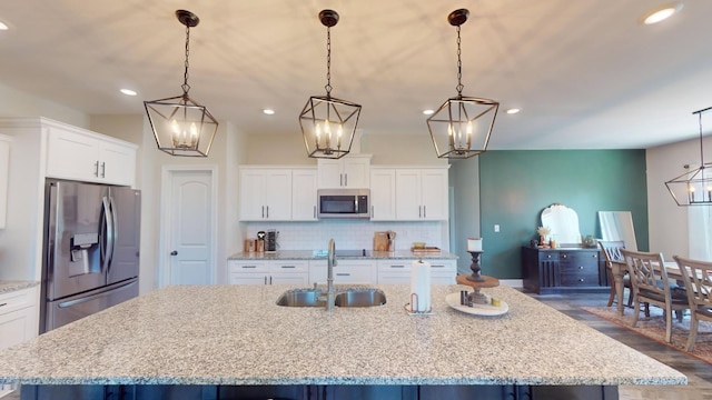 kitchen featuring white cabinets, a large island with sink, backsplash, a sink, and appliances with stainless steel finishes