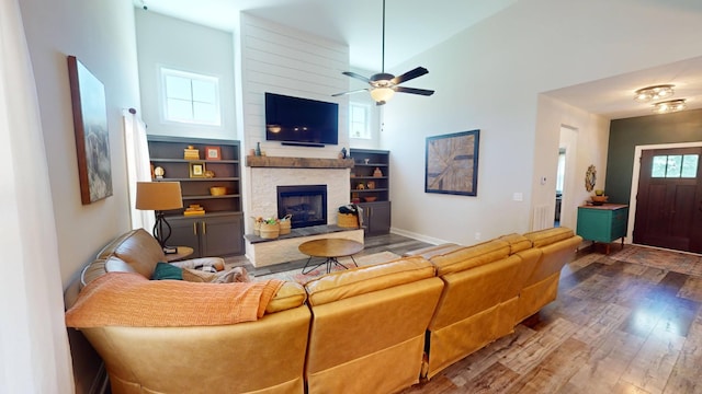 living area featuring a ceiling fan, wood finished floors, a high ceiling, a fireplace, and baseboards