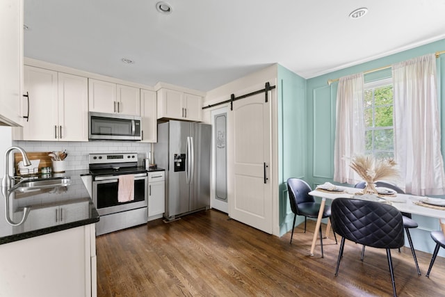 kitchen featuring a barn door, white cabinets, stainless steel appliances, a sink, and tasteful backsplash