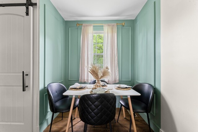 dining space with a barn door, a decorative wall, and wood finished floors