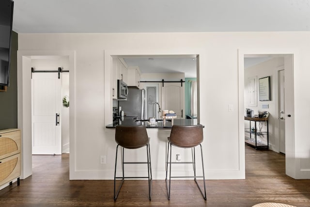 kitchen featuring a kitchen bar, a barn door, white cabinetry, and appliances with stainless steel finishes