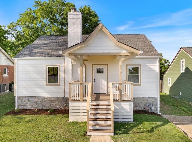 bungalow-style home featuring a shingled roof, a front lawn, fence, and a chimney