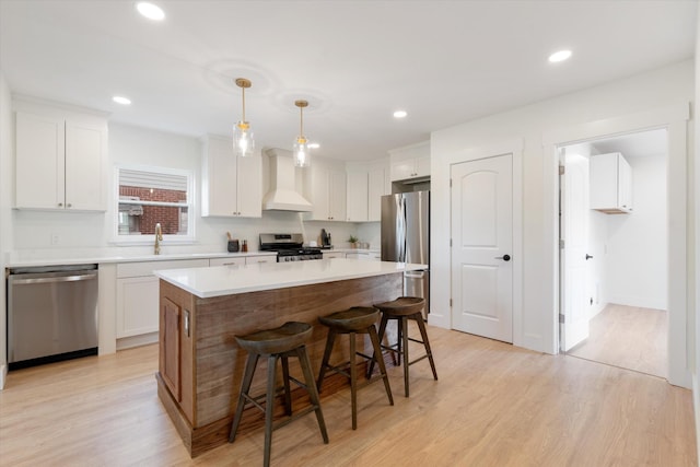 kitchen featuring white cabinets, appliances with stainless steel finishes, a sink, a kitchen breakfast bar, and premium range hood