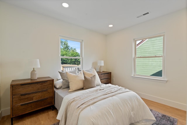 bedroom featuring visible vents, baseboards, wood finished floors, and multiple windows
