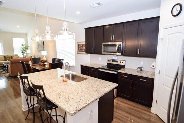 kitchen featuring a sink, stainless steel appliances, a kitchen bar, dark wood-style flooring, and visible vents