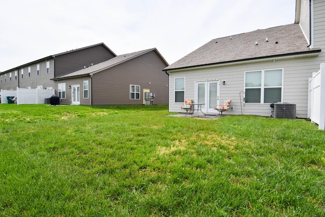 rear view of property featuring fence, a lawn, and central air condition unit