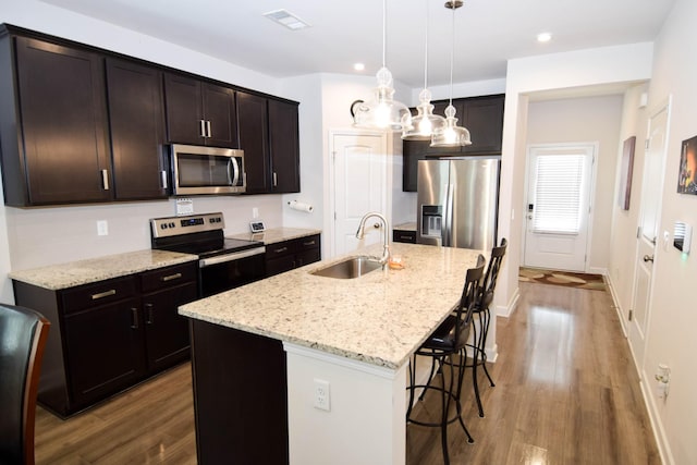 kitchen with stainless steel appliances, a sink, visible vents, wood finished floors, and a breakfast bar area