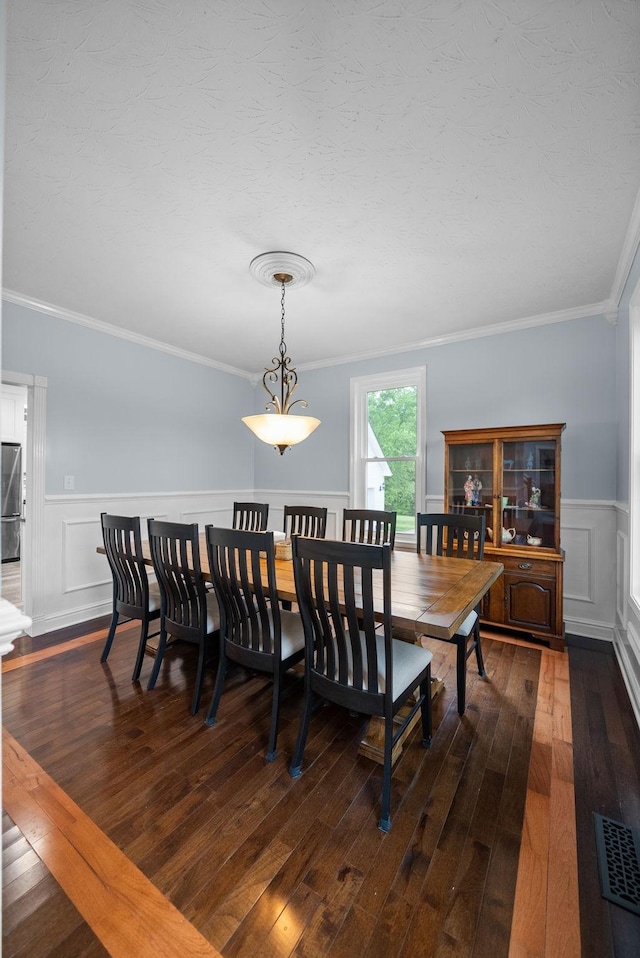 dining room featuring dark wood finished floors, visible vents, ornamental molding, a decorative wall, and wainscoting