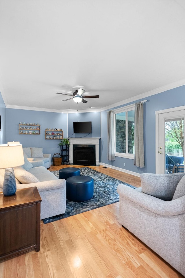 living room with a fireplace, crown molding, wood finished floors, and a ceiling fan