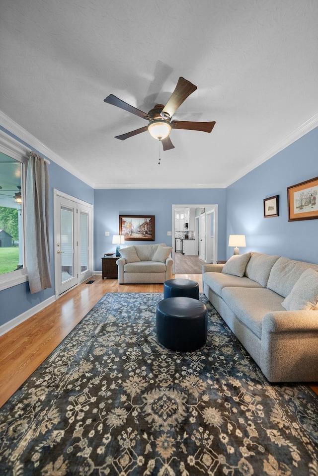 living area featuring ornamental molding, baseboards, a ceiling fan, and wood finished floors