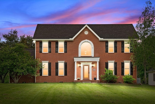 colonial inspired home featuring brick siding, roof with shingles, and a front yard