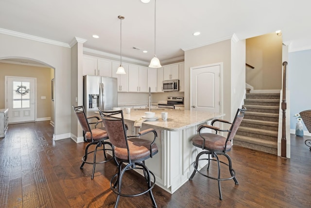 kitchen featuring stainless steel appliances, arched walkways, white cabinetry, light stone countertops, and ornamental molding