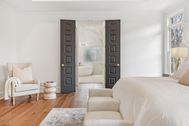 bedroom with wood finished floors, crown molding, baseboards, and ensuite bathroom