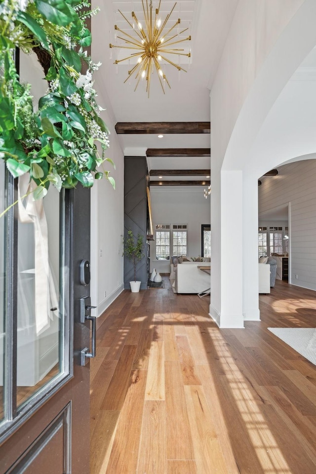 foyer with arched walkways, baseboards, a notable chandelier, beamed ceiling, and wood finished floors