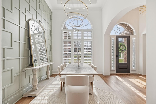 entryway with arched walkways, a chandelier, wood finished floors, and crown molding