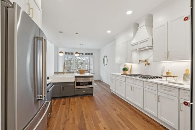 kitchen with hardwood / wood-style floors, stainless steel appliances, light countertops, custom range hood, and white cabinetry