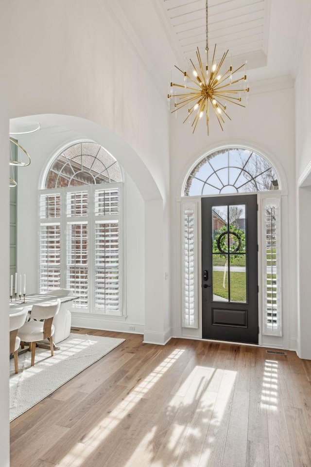 entrance foyer with arched walkways, a towering ceiling, a chandelier, ornamental molding, and wood-type flooring