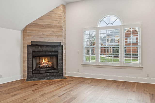 unfurnished living room featuring a fireplace with flush hearth, vaulted ceiling, wood finished floors, and baseboards